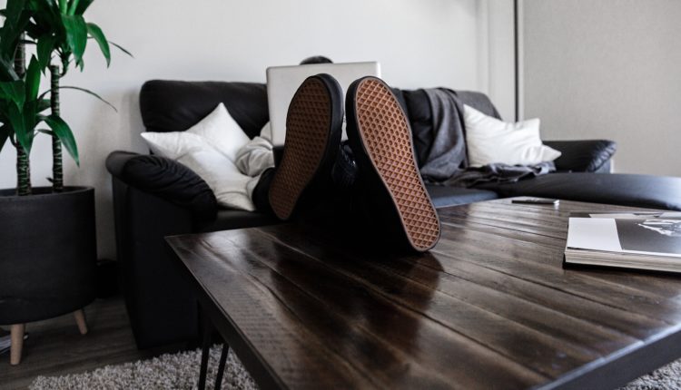 person sitting on sofa resting its feet on top of coffee table while using laptop