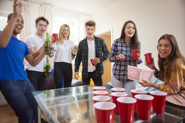 a mixed group of students sharing a house, have a pre-drinks party in their flat. They are drinking and dancing and messing about playing beer pong...