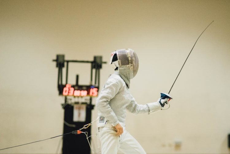 man wearing white coveralls holding fencing sword