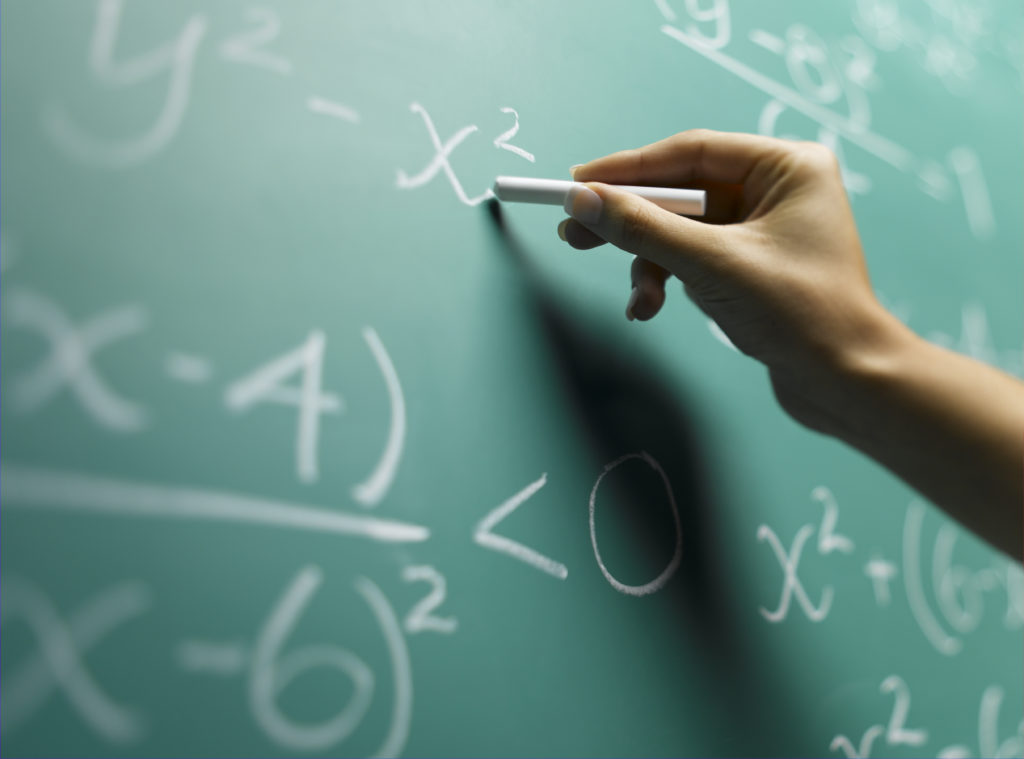 Young woman writing on blackboard, close-up of hand (focus on hand)