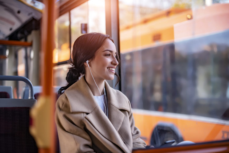 One Young Woman Smiling in a Bus While Listening to Music using Earphones. Beautiful Young Woman With Earphones Taking Bus to Work. The Passenger L...