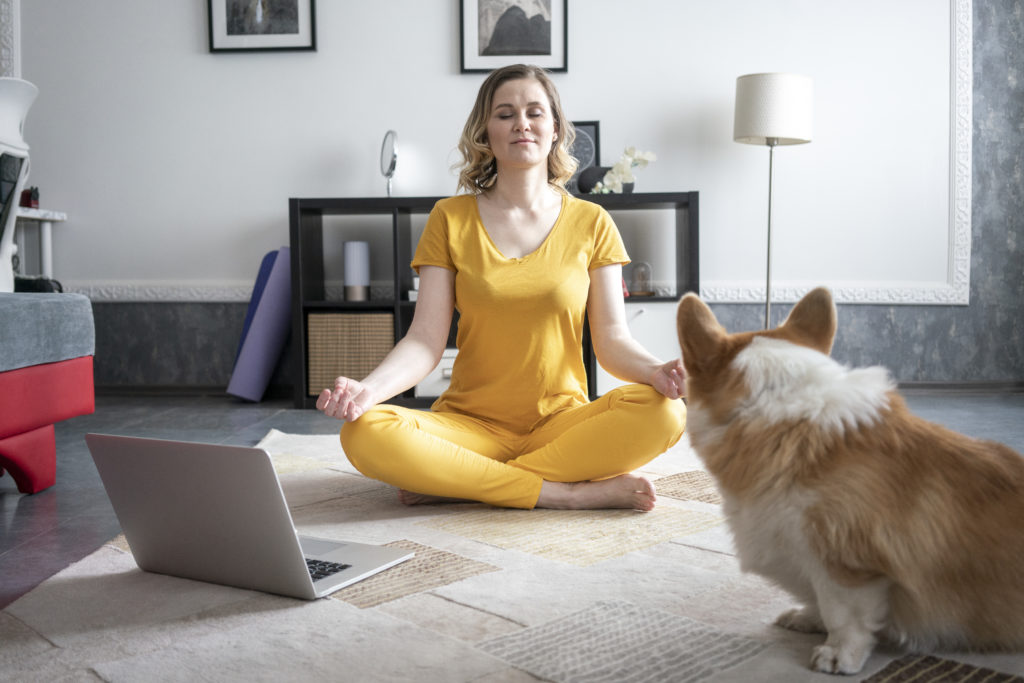 Woman with dog practising yoga in living room at home
