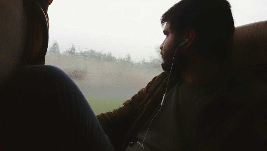 Man Listening To Music Sitting In Bus While Looking Through Window