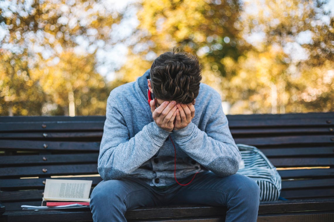 Teenager sits on a bench in the park and listen to music and learning for exame