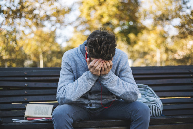 Teenager sits on a bench in the park and listen to music and learning for exame