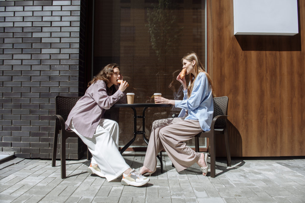 two young women sit in a cafe eating and chatting while having fun together