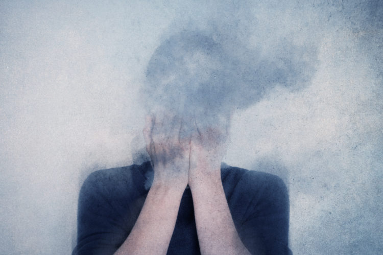 A mental health concept. Of a man with his head in his hands vanishing into clouds. With a texture edit