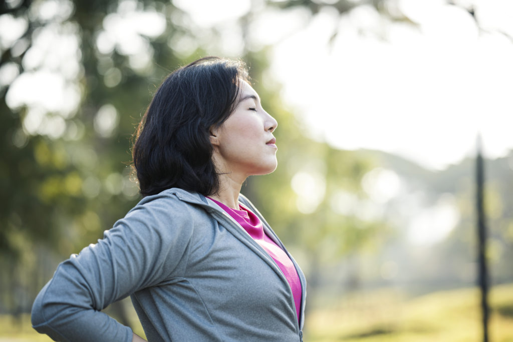 Rest and Recovery After Exercise. Side View of Asian working women take a rest after outdoors workout in a city park.