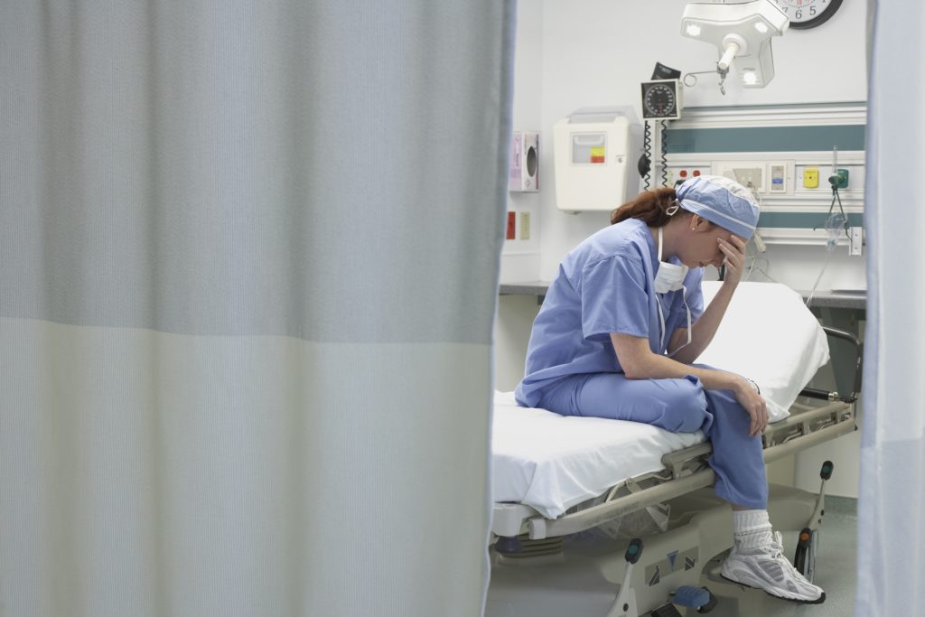 View through privacy curtains to female doctor sitting with head in hand