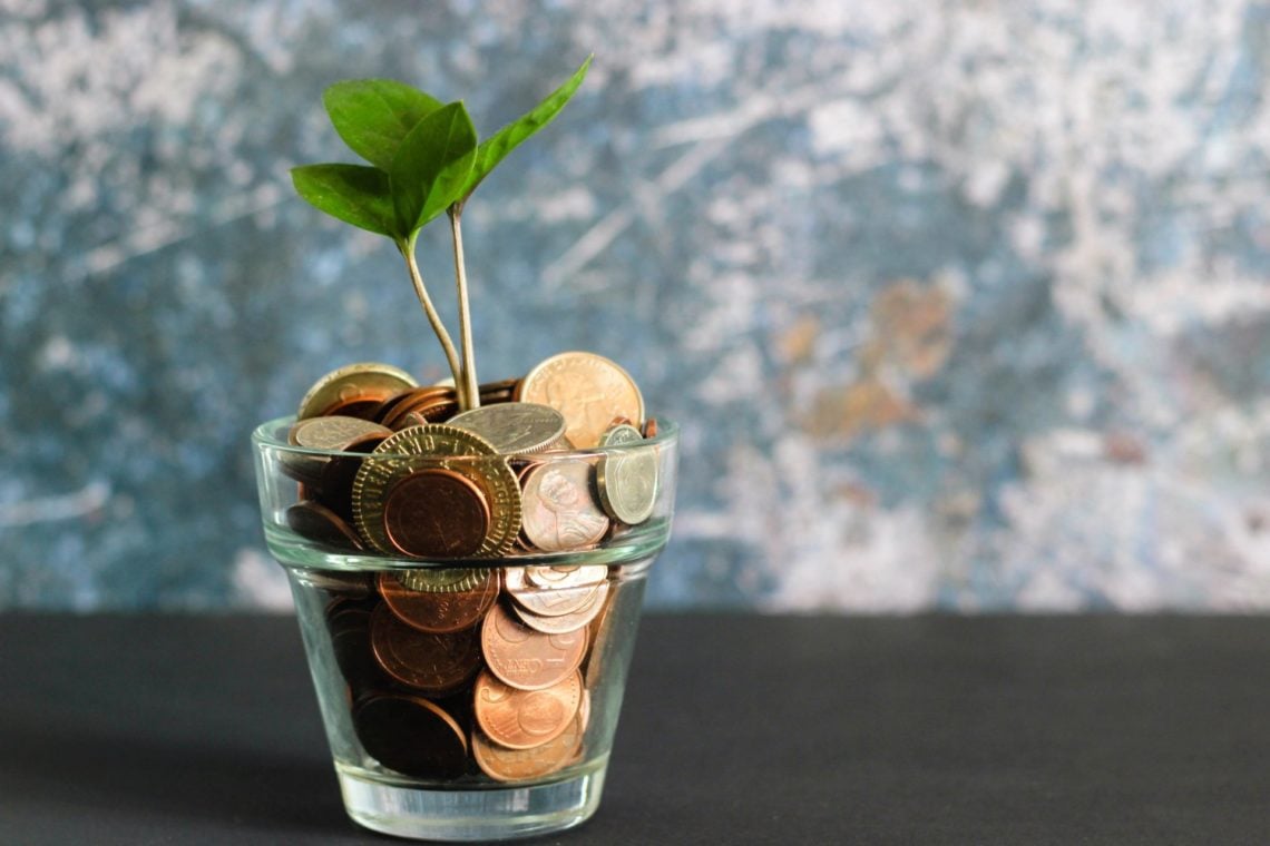 small green plant growning from glass pot full of coins