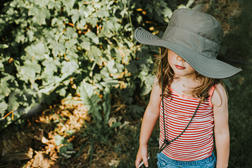 Cute young child wearing a strappy top and a wide brim khaki hat to protect her from the sun. Her face is partly obscured and she is expressionless...