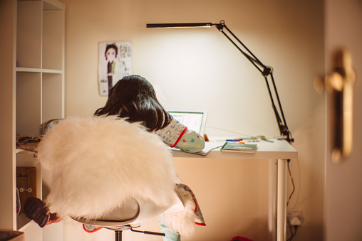 Rear view of little girl using digital tablet for learning in her study room at home
