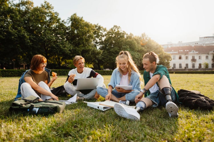 Disabled man with classmates discussing college project outside in park.