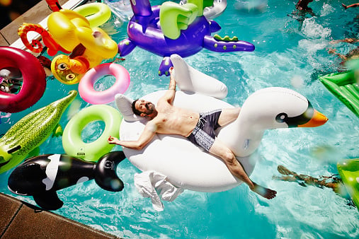 Smiling man relaxing on inflatable swan in pool