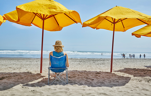 Rear view of female tourist sitting under beach umbrella, Camana, Arequipa, Peru