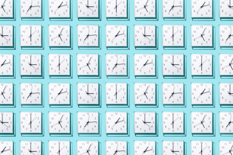 Neatly Arranged White Colored Wall Clocks Displays Different Time on Solid Blue Background.