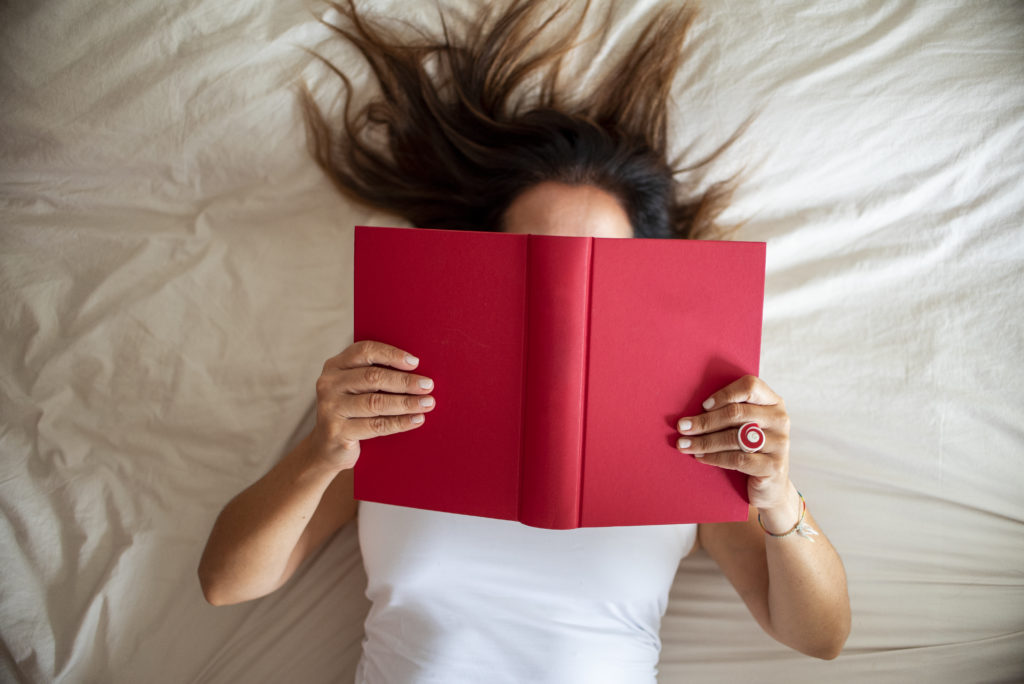 Woman reading a book with the face covered by the book.