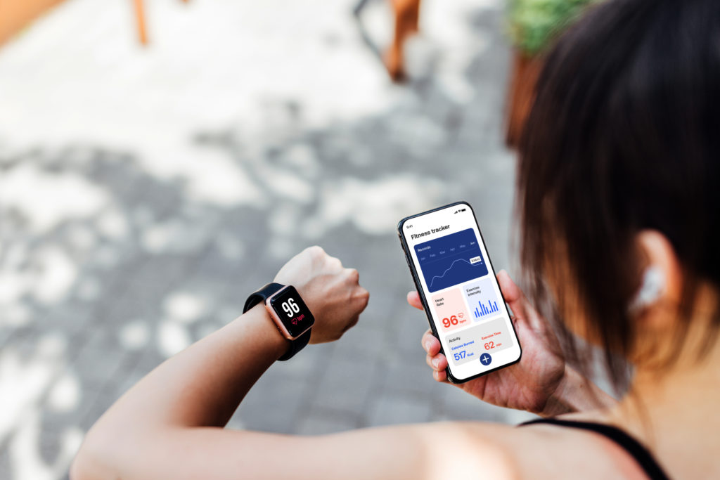 Young Woman Using Fitness Tracker App On Smart Watch And Smartphone