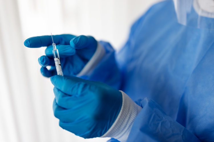 Close-up of a doctor hand wearing protective gloves preparing coronavirus vaccine syringe. Healthcare worker with a vaccination injection.
