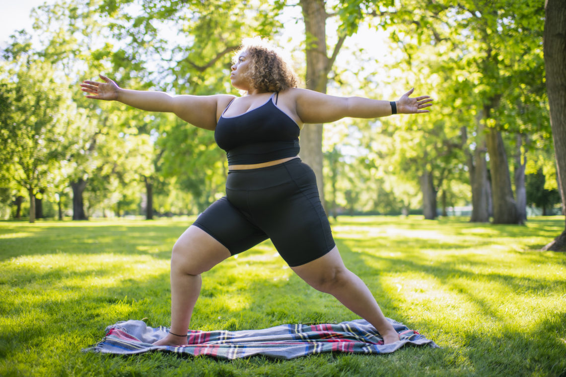 Young woman practicing yoga doing Virabhadrasana II or Warrior 2 Pose outdoors in park