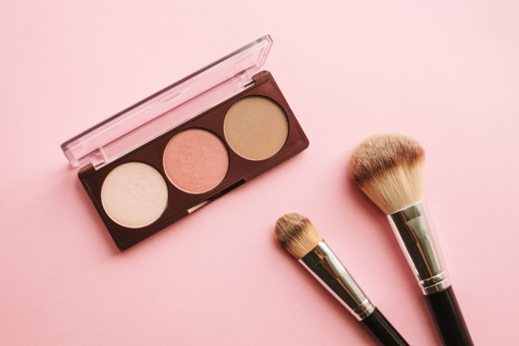 Face powder, blusher and highlighter palette of nude colors over pink background