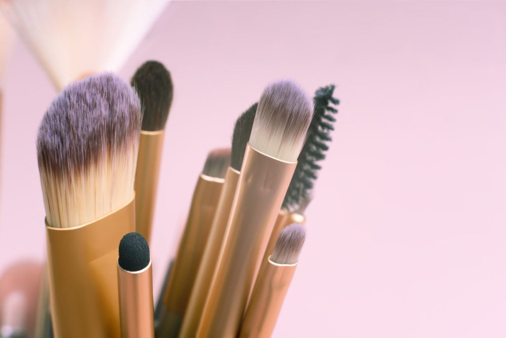 Top view close up of many cosmetic make-up brushes on pink background.