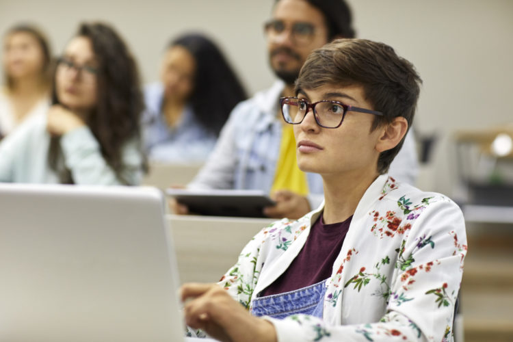 Young student with laptop studying in university. Female is concentrating in classroom. She is in casuals.