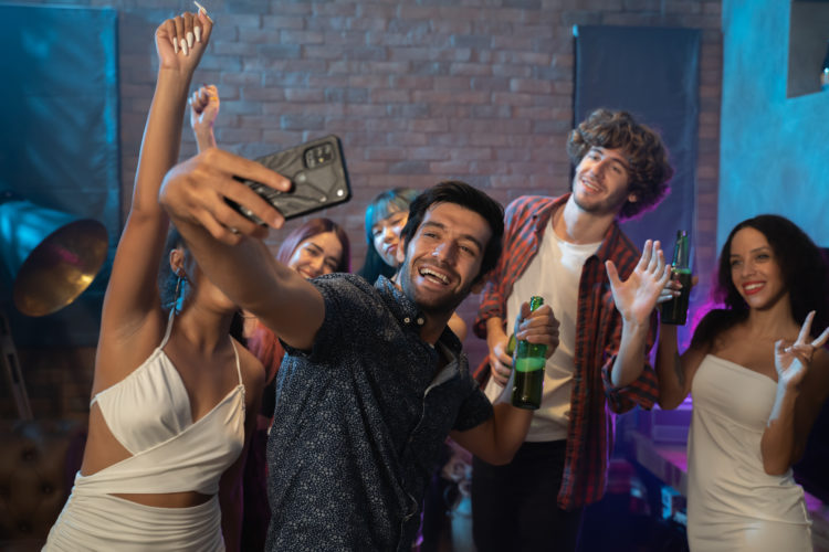 Diverse group of young people dancing at the night club, and taking a selfie with smartphone