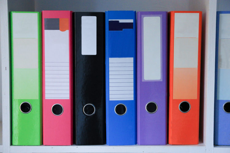 Row of brightly coloured A4 lever arch files on a white shelf used for storing documents.