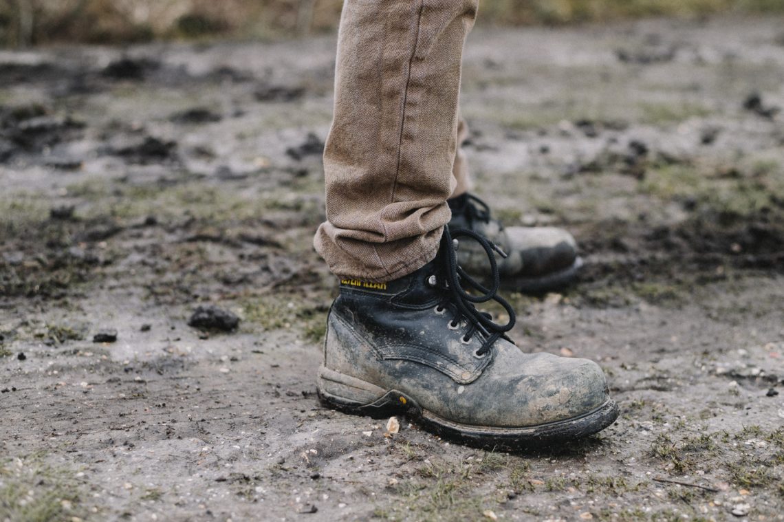 person in black work shoes standing on dirt pathway