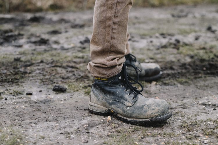 person in black work shoes standing on dirt pathway