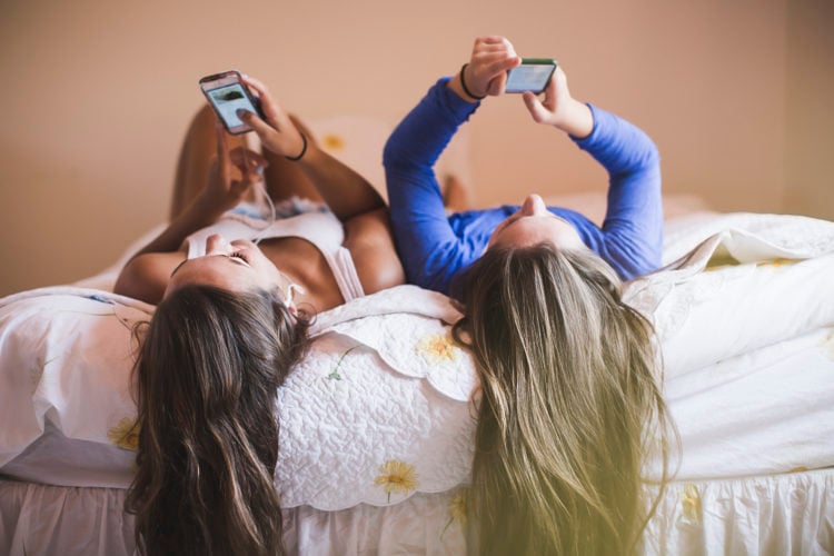 Teenage girls lying on bed looking at smart phones. Credit: Getty