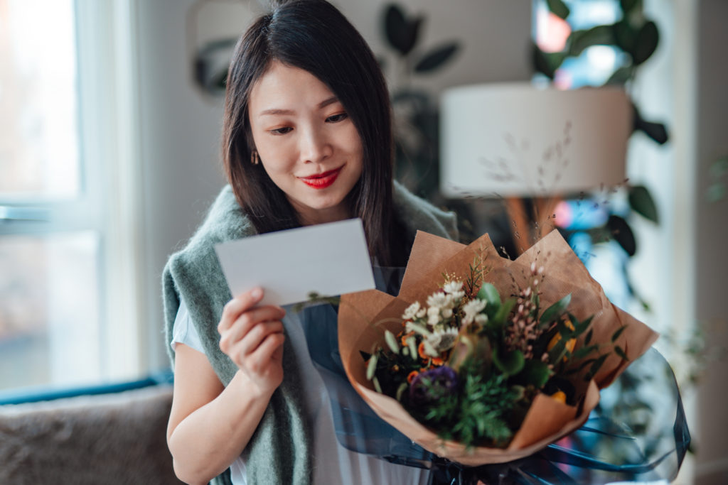 Young Asian woman reading greeting card attached and holding flower bouquet
