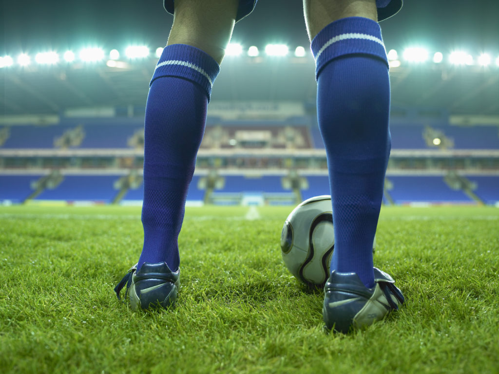 Young male football player on pitch, low section, night