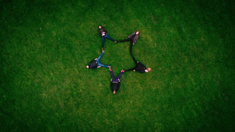 five people laying on grass field making star sign