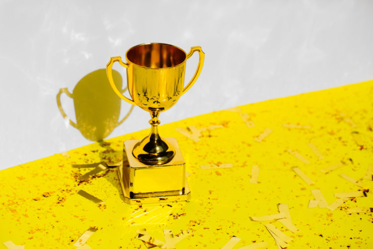 Golden champions cup standing on yellow background with glitter and confetti. Trendy colors of 2021 year