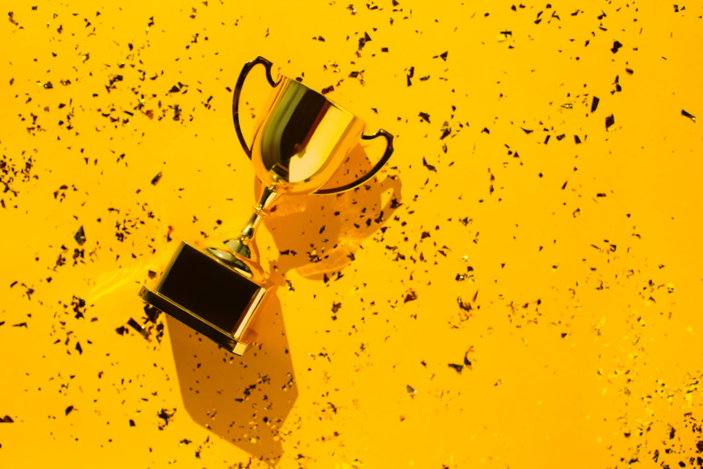 Top view of metallic golden goblet on bright yellow background with sequin. Goal achievement concept. Trendy colors of the year