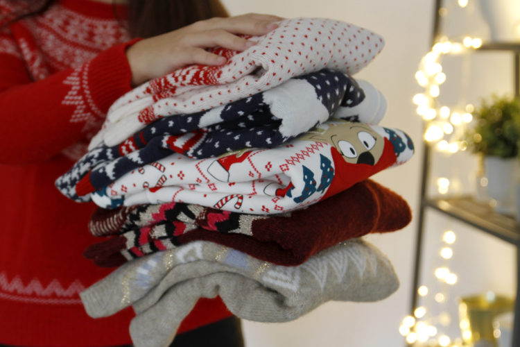 Woman holding stack of folded Christmas sweaters