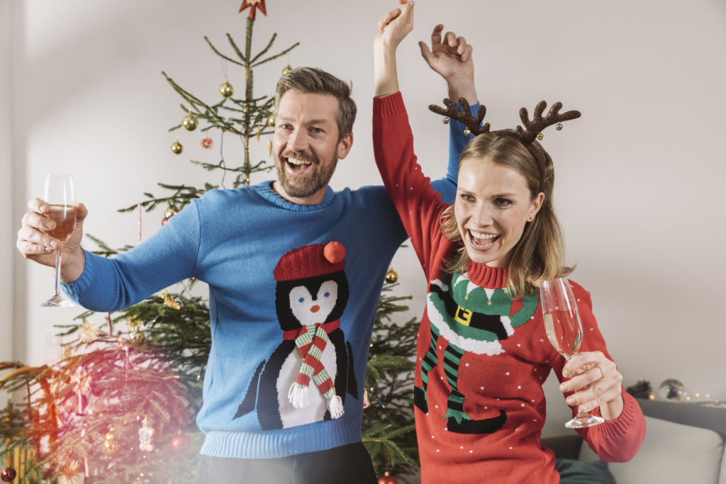 Two people with ugly Christmas sweaters dancing in front of tree