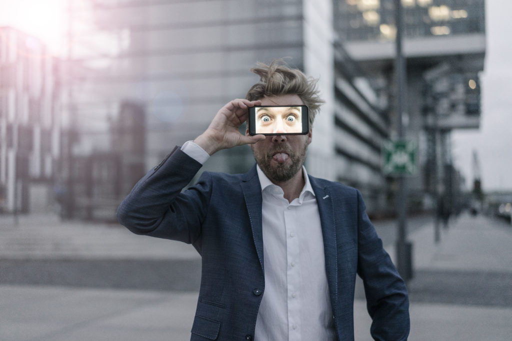 Playful businessman holding cell phone in front of his eyes