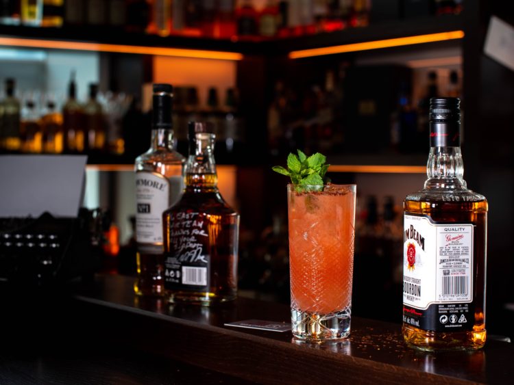 three liquor bottles and cocktail drink on bar counter
