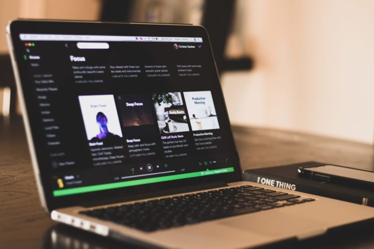 spotify web displayed on open macbook on wooden table next to book and phone