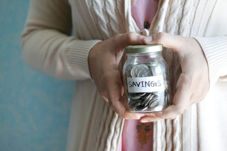 A clear jar filled with coins labelled savings held up to camera