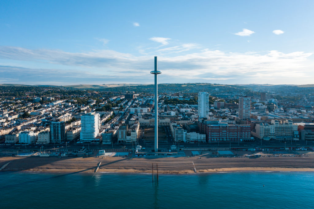 Aerial Shot Of Brighton With The I360 And Beach In The Morning Light With Wispy Cloud And Blue Sky