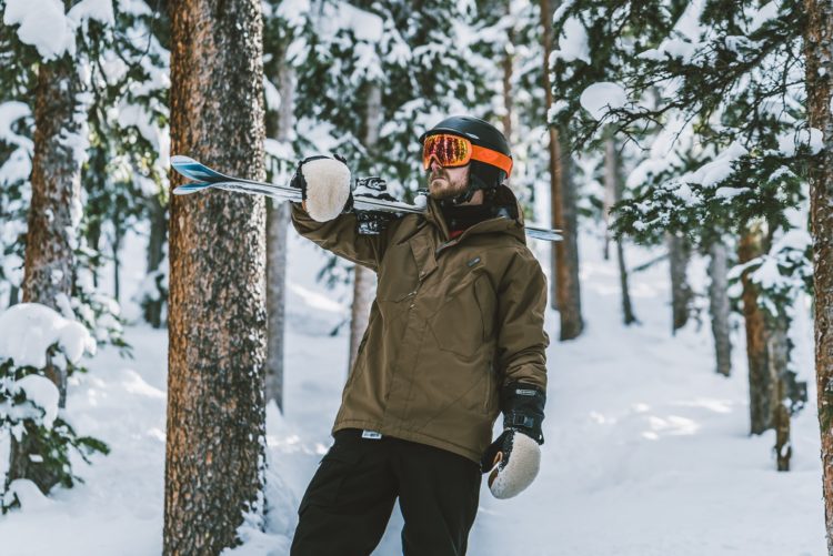 man in brown jacket and black pants holding black and white snow ski pole