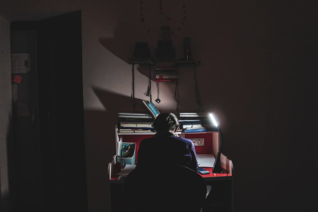 man in black shirt sitting on chair using computer in the dark.