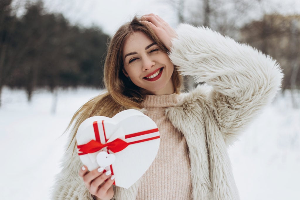 Young woman holding white heart shaped box.