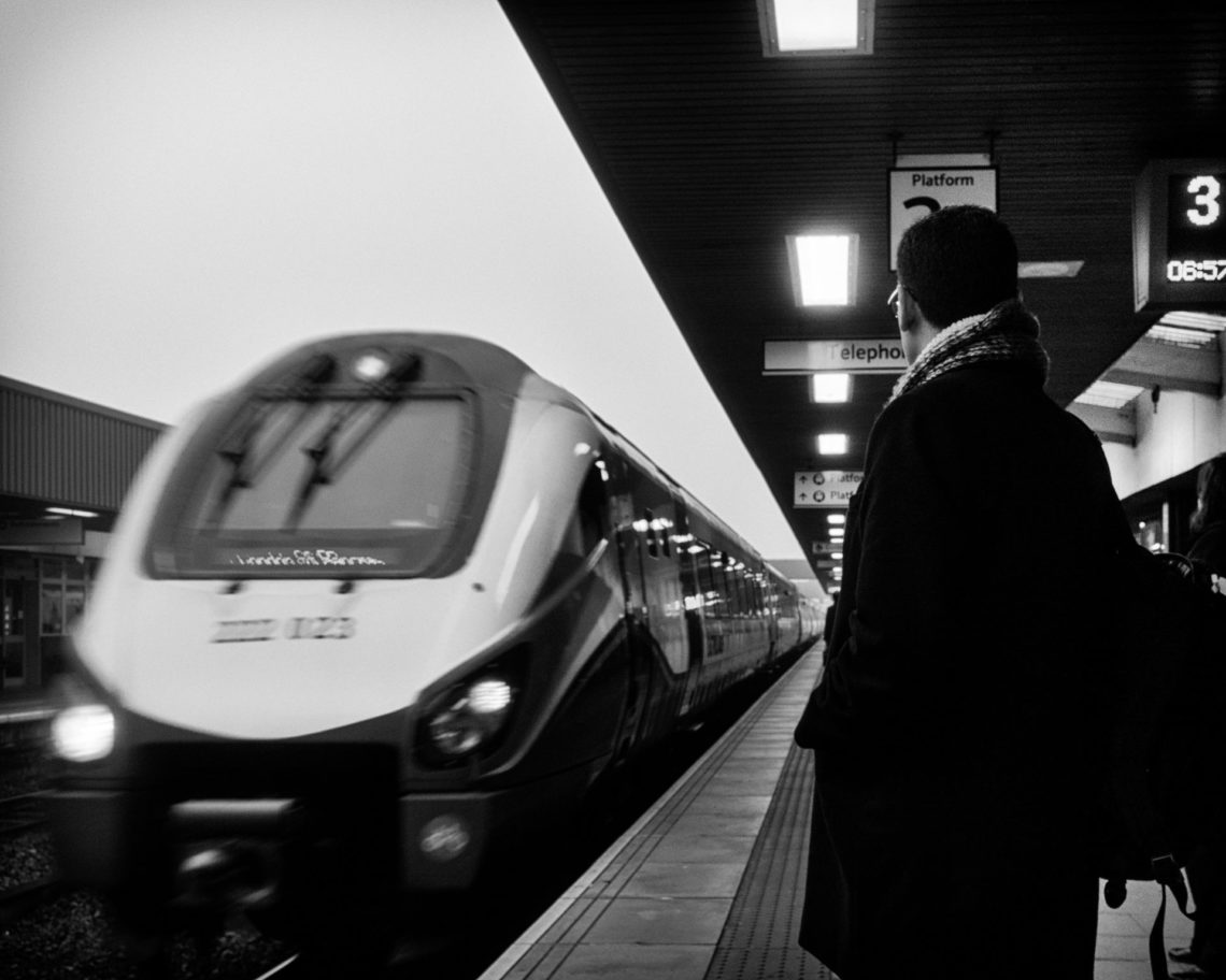 black and white photo of man standing beside moving train