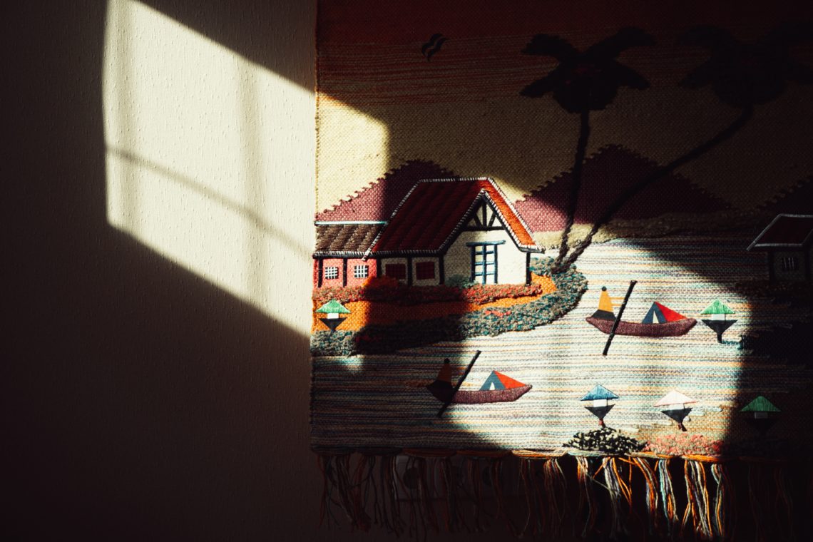 a tapestry with a house and boats hanging on a wall