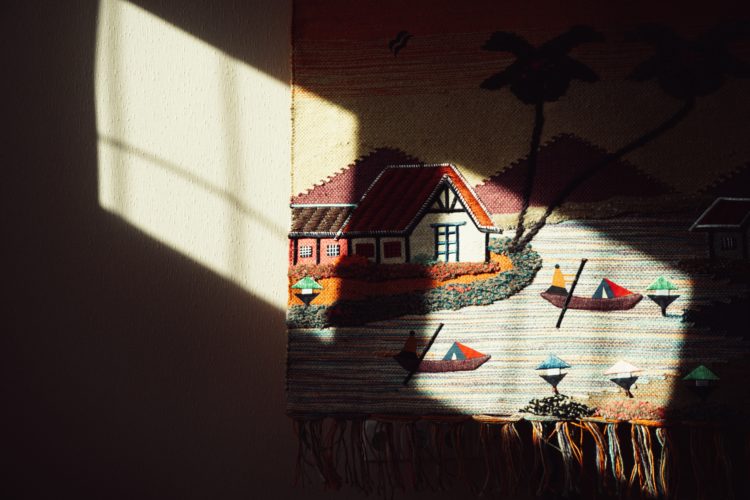 a tapestry with a house and boats hanging on a wall